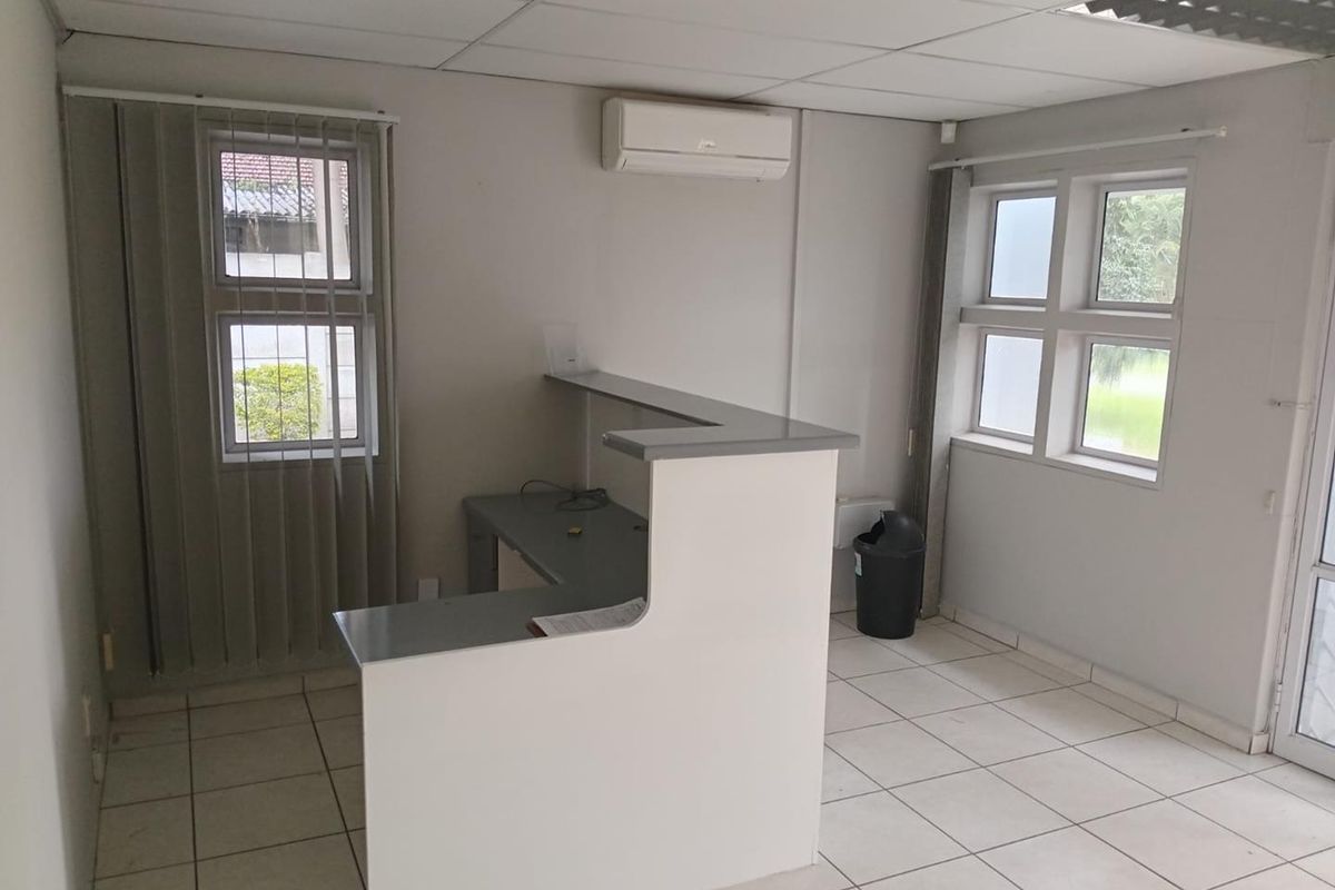 A functional office space featuring a built-in reception desk, tiled flooring, suspended ceiling, and a wall-mounted air conditioning unit.