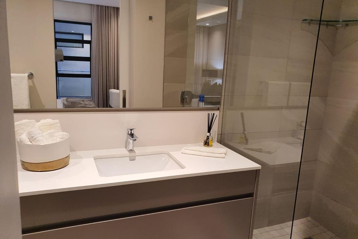 Modern bathroom featuring a floating vanity with integrated basin, large wall mirror, and a glass-enclosed walk-in shower with neutral tiling.