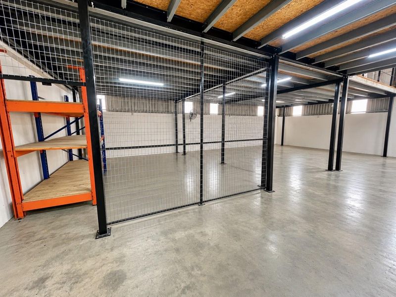Spacious industrial utility area featuring concrete flooring, steel mezzanine structure, and secure wire mesh partitioning, suitable for storage or workshop use.
