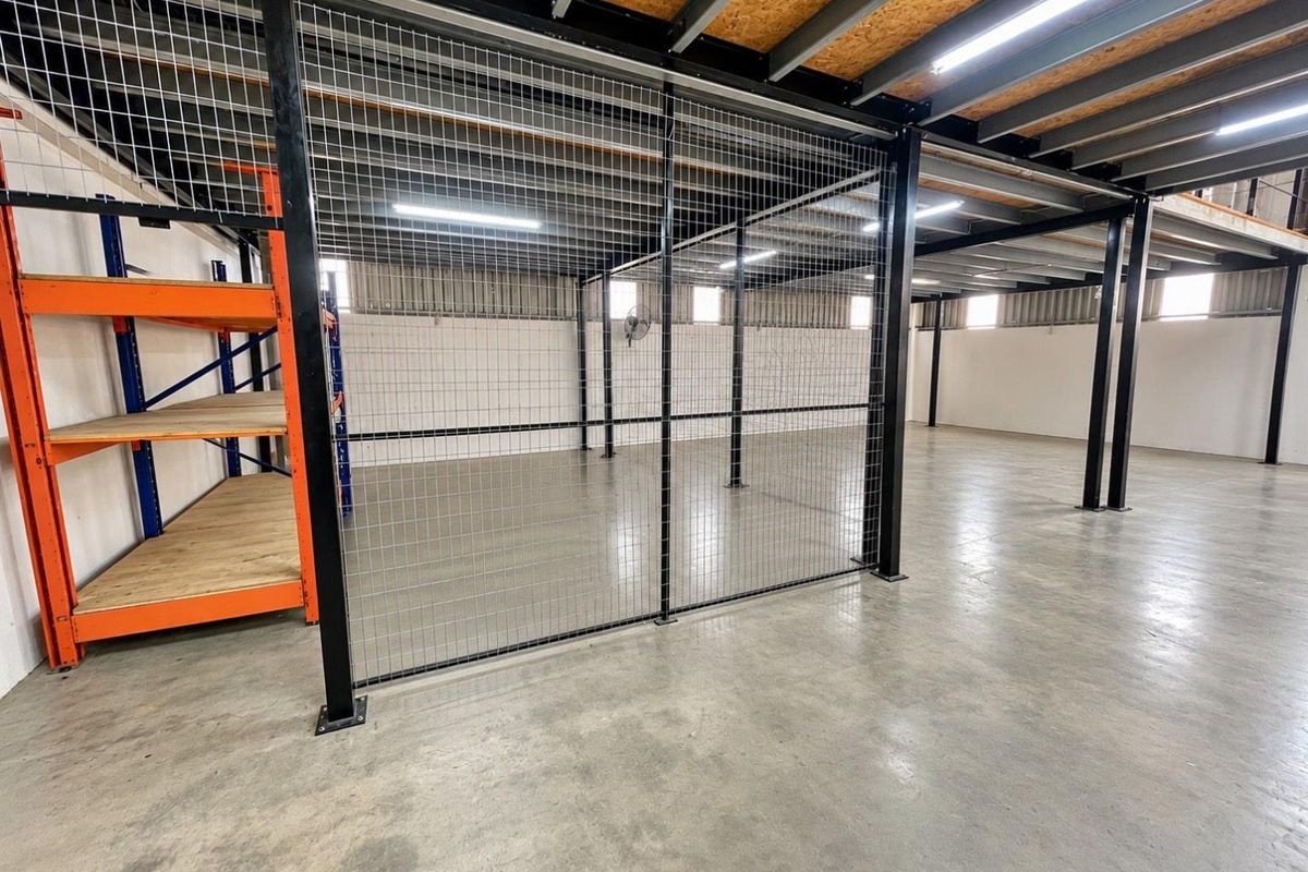 Spacious industrial utility area featuring concrete flooring, steel mezzanine structure, and secure wire mesh partitioning, suitable for storage or workshop use.