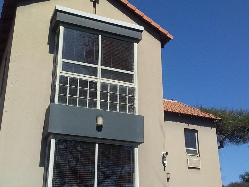 Rear elevation of a multi-story building featuring terracotta roof tiles, security camera, and large windows with security bars.