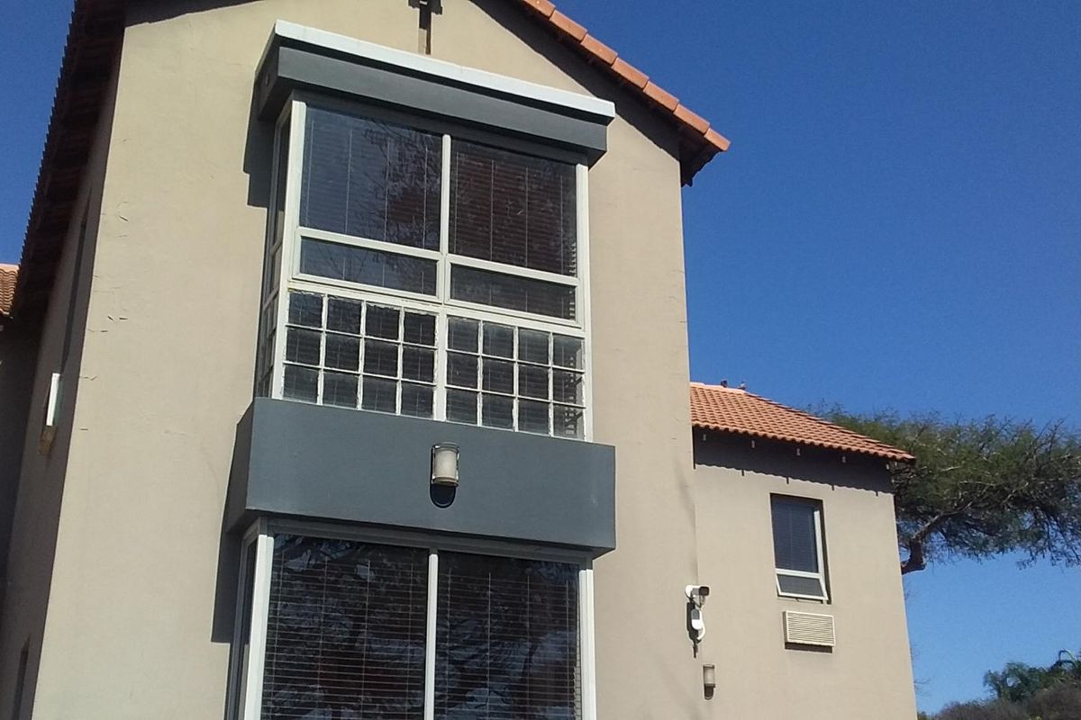 Rear elevation of a multi-story building featuring terracotta roof tiles, security camera, and large windows with security bars.