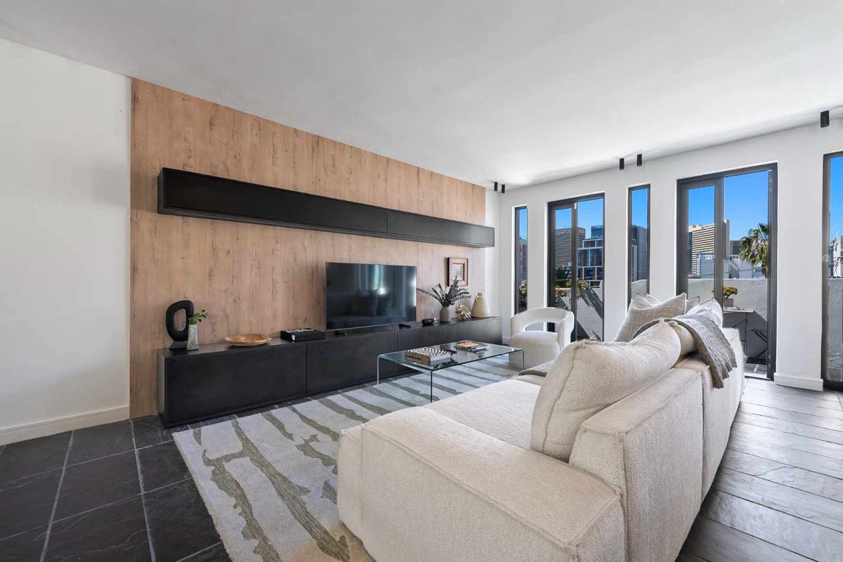 Modern living room featuring sleek built-in cabinetry, dark stone tile flooring, and large windows providing ample natural light and urban views.