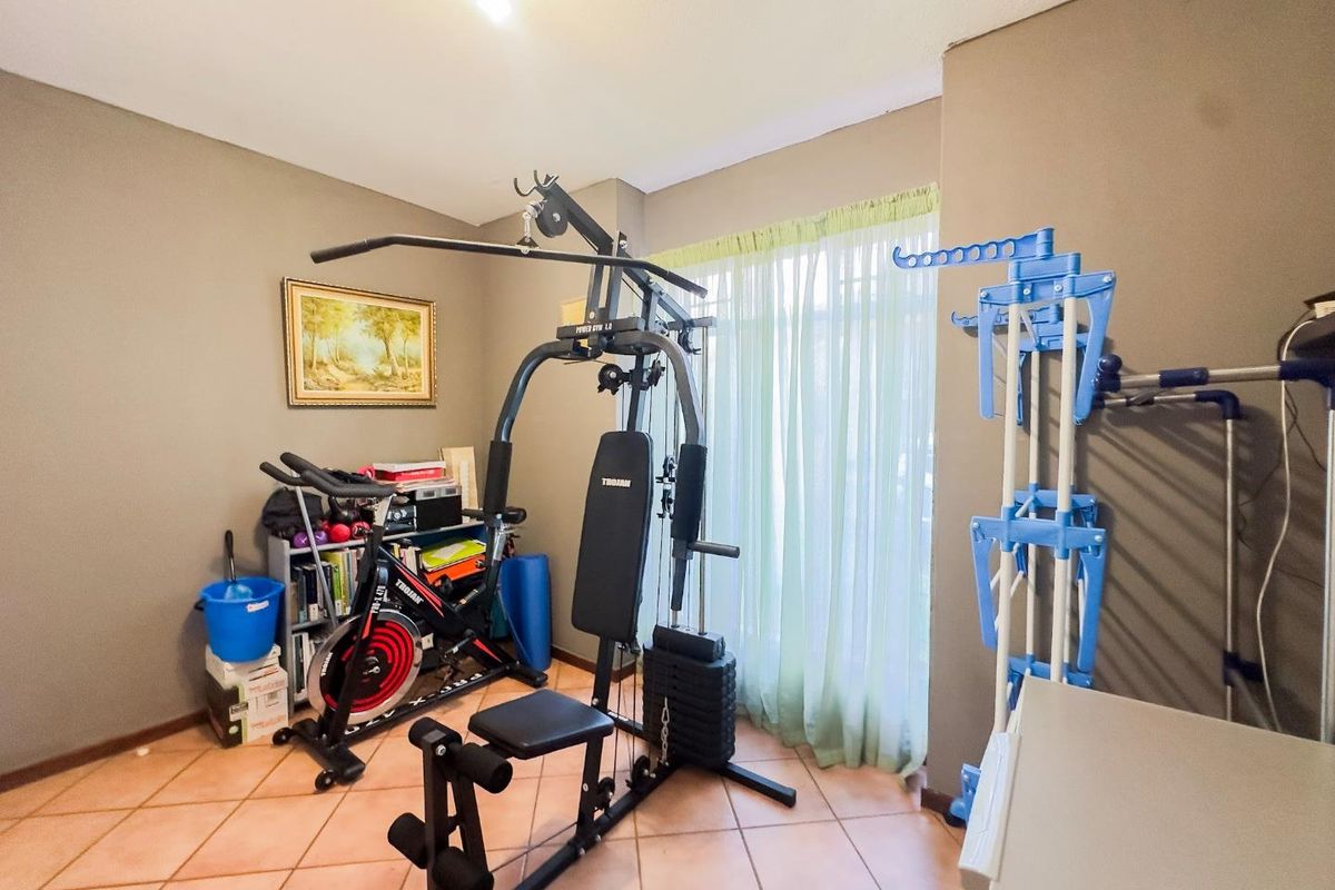 A multi-purpose room featuring tiled flooring and a window with curtain rails, currently utilized as a home gym space.