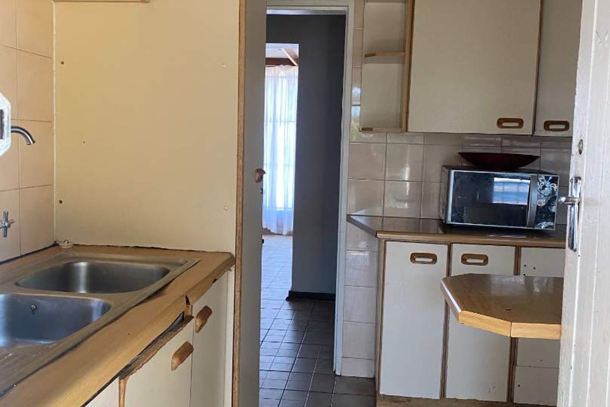A dated kitchen featuring tiled flooring, laminate cabinetry, and a double bowl stainless steel sink, offering potential for a modern renovation.