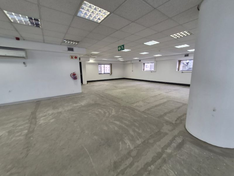 An open-plan office space featuring a suspended ceiling, recessed lighting, air conditioning, and an unfinished concrete floor, ready for tenant-specific flooring installation.