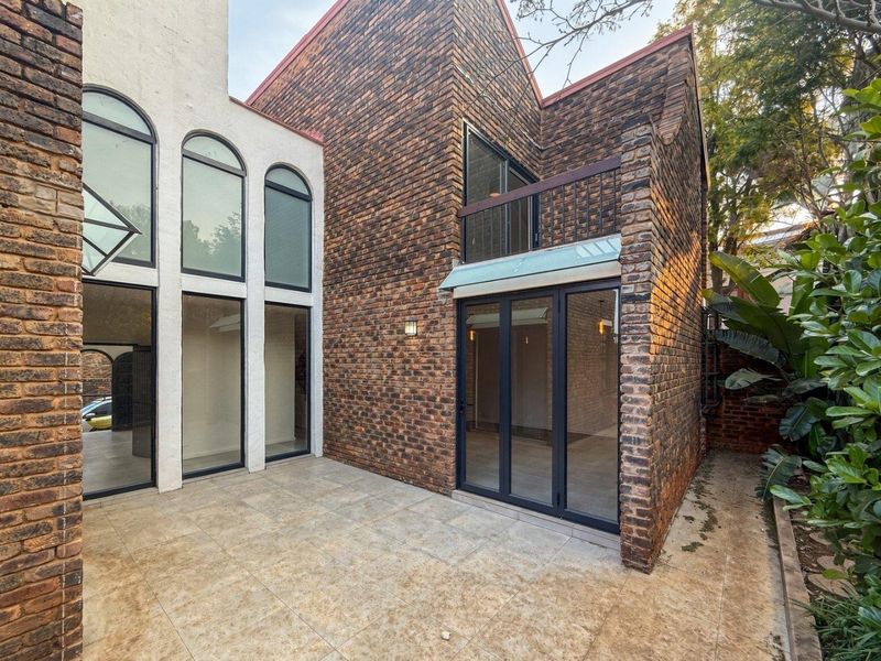 Rear exterior view of a townhouse featuring a tiled patio, exposed brickwork, arched windows, and a small balcony with bi-fold door access.