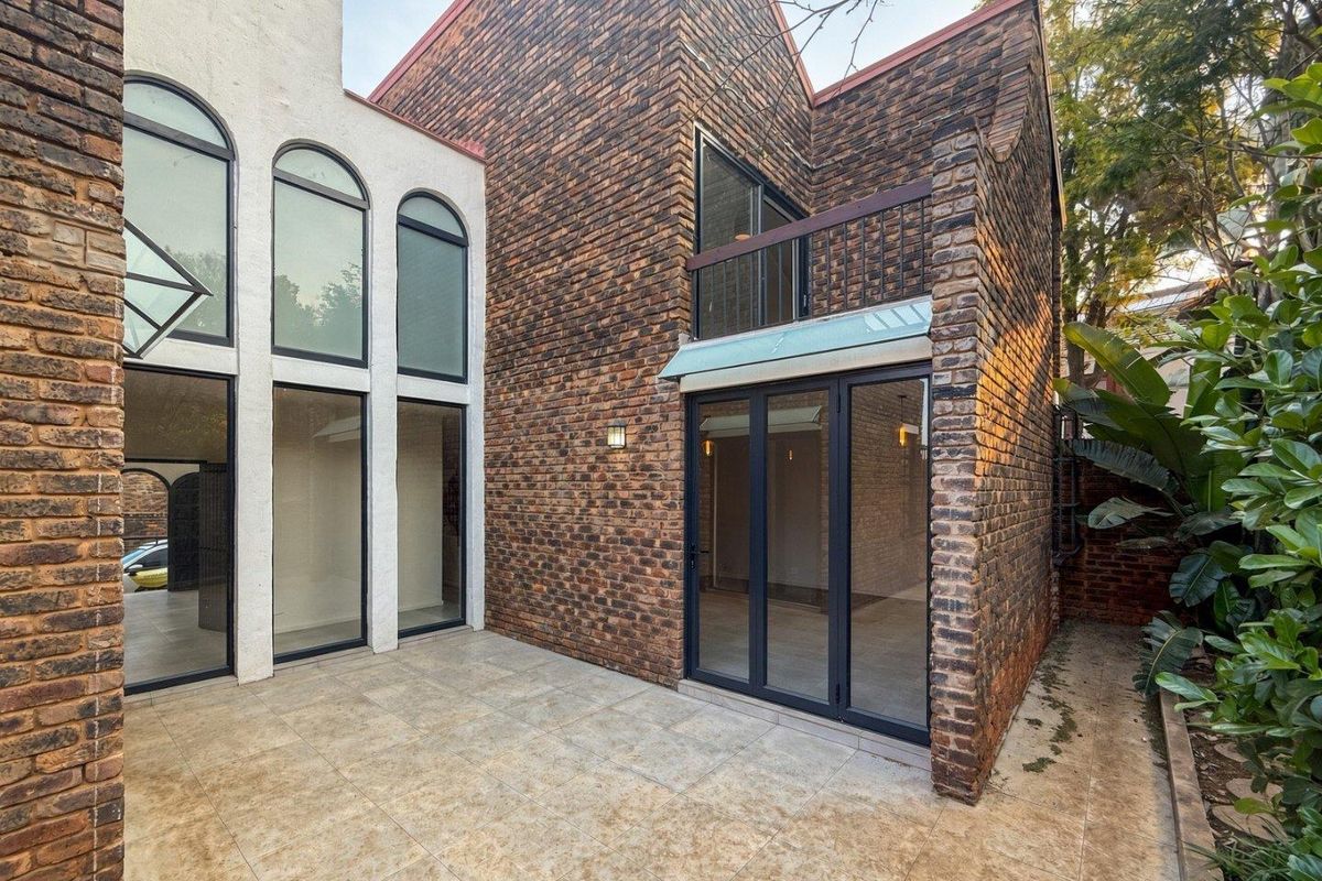 Rear exterior view of a townhouse featuring a tiled patio, exposed brickwork, arched windows, and a small balcony with bi-fold door access.