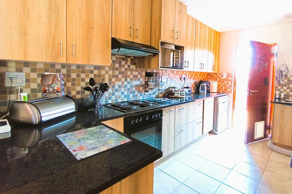 A functional kitchen featuring light wood cabinetry, dark granite countertops, a built-in oven with extractor fan, and a tiled backsplash.