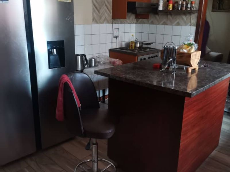 A functional kitchen featuring a central island, built-in cabinetry, tiled backsplash, and modern laminate flooring, providing a practical workspace for daily cooking.