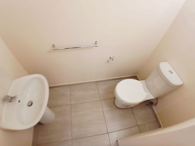 A clean and functional guest bathroom featuring a pedestal washbasin, a standard toilet, and neutral floor tiling.