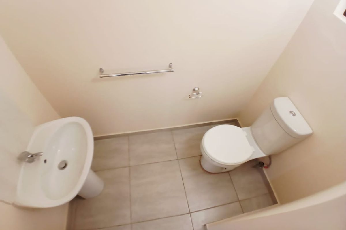 A clean and functional guest bathroom featuring a pedestal washbasin, a standard toilet, and neutral floor tiling.