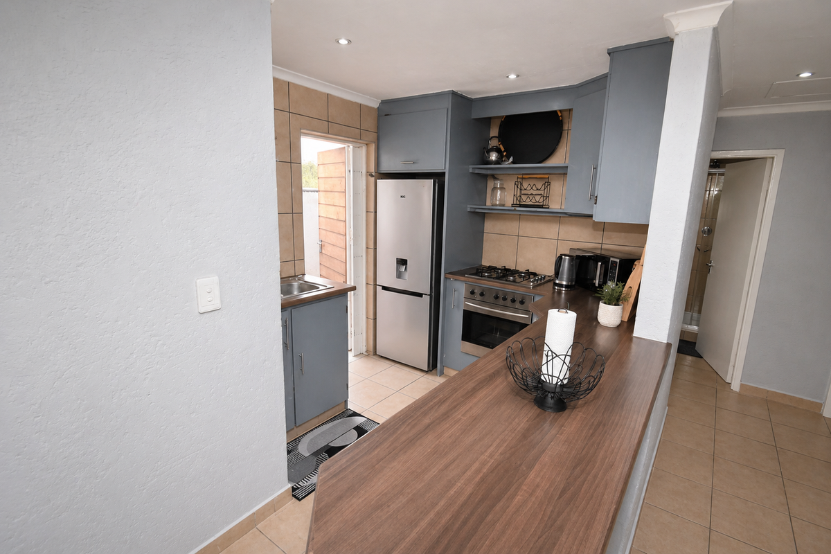 Compact kitchen featuring blue cabinetry, wood-look breakfast bar, built-in oven, gas hob, and tiled flooring with direct access to an outdoor area.