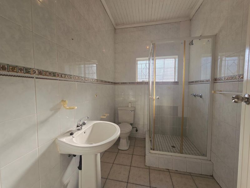 A functional bathroom featuring a pedestal basin, toilet, and a glass-enclosed shower with tiled walls and flooring.