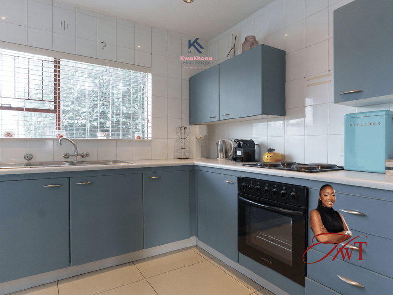 A functional kitchen featuring blue cabinetry, tiled splashbacks, a built-in oven, and a stainless steel sink with a window view.