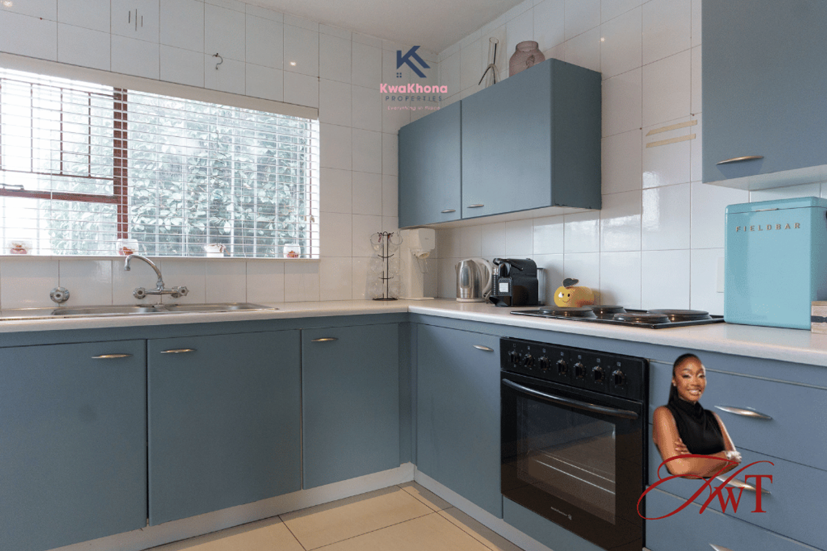 A functional kitchen featuring blue cabinetry, tiled splashbacks, a built-in oven, and a stainless steel sink with a window view.