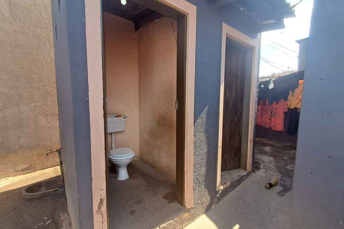 An outdoor toilet facility featuring a basic porcelain toilet and cistern, located in a utilitarian exterior area.