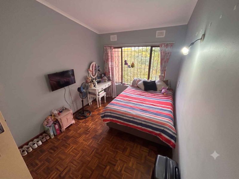 A bedroom featuring parquet flooring, a large window with security bars, and a wall-mounted light fixture.