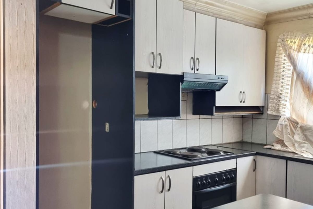 A dated kitchen featuring built-in cabinetry, laminate countertops, an integrated oven and hob, and tiled flooring, offering potential for a modern renovation.