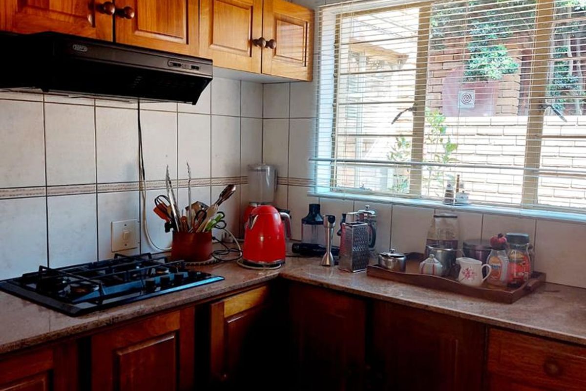 A functional kitchen featuring wooden cabinetry, a built-in gas hob, extractor fan, and tiled splashbacks with natural light from a window.