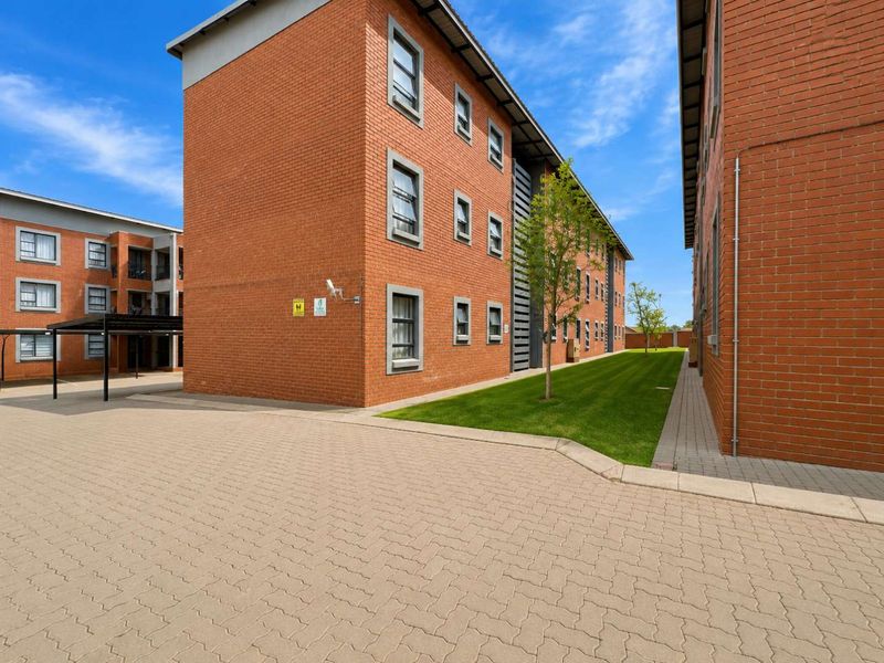 Exterior view of a multi-story brick apartment complex featuring a paved driveway, manicured lawn, and covered parking area.