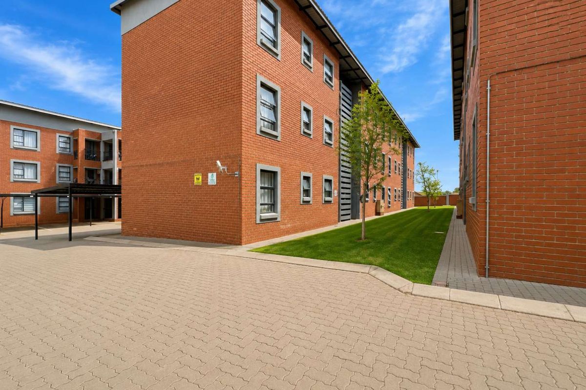 Exterior view of a multi-story brick apartment complex featuring a paved driveway, manicured lawn, and covered parking area.