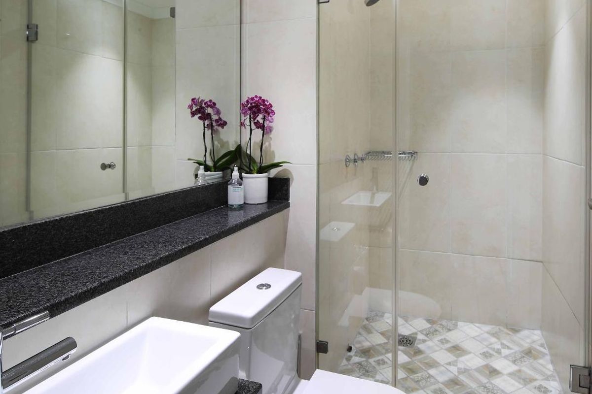 Modern bathroom featuring a glass-enclosed shower with patterned floor tiles, a sleek vanity with a stone countertop, and a wall-mounted mirror.