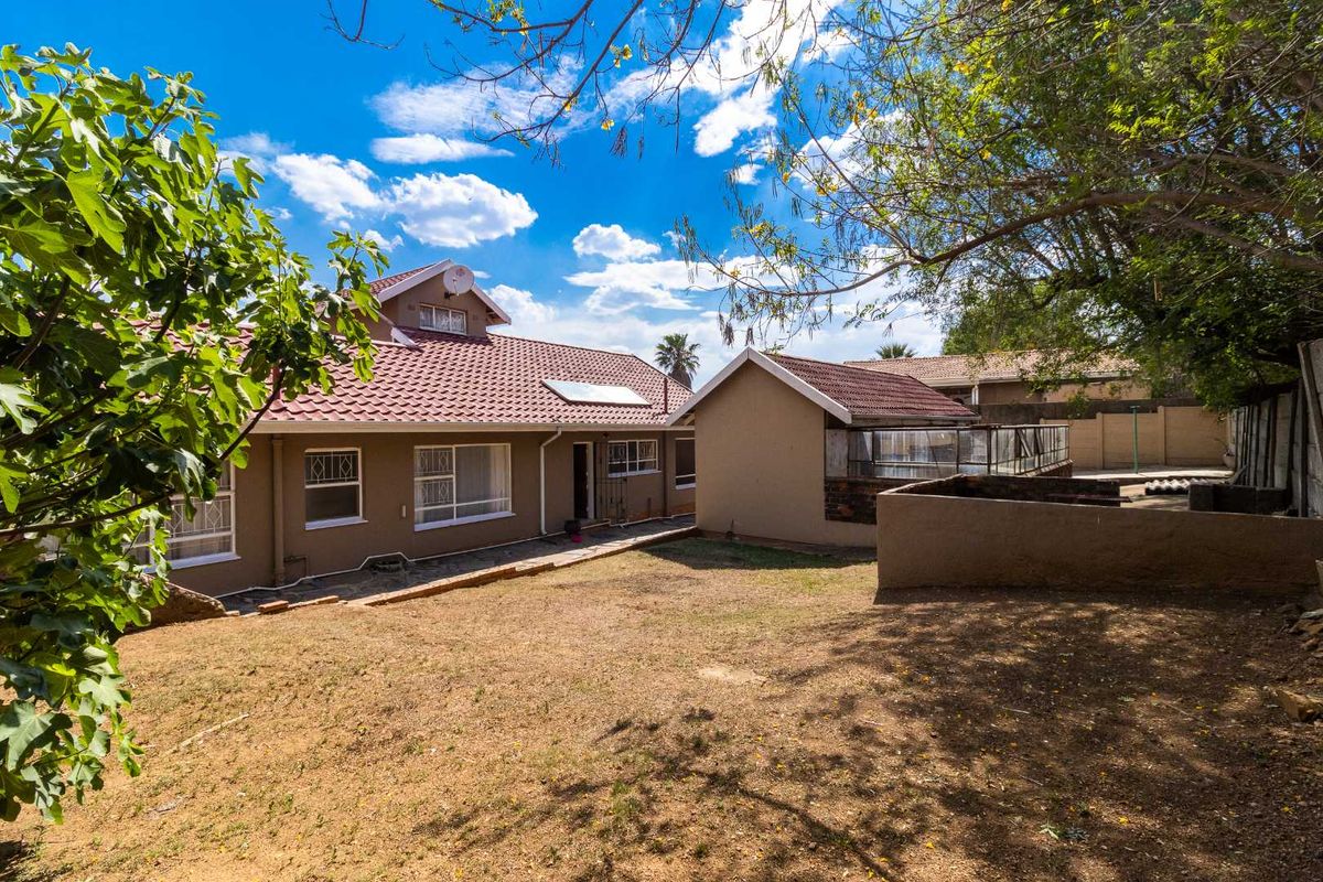 Rear view of the house featuring a tiled roof, solar water heating panel, and a spacious backyard area with a small outbuilding.