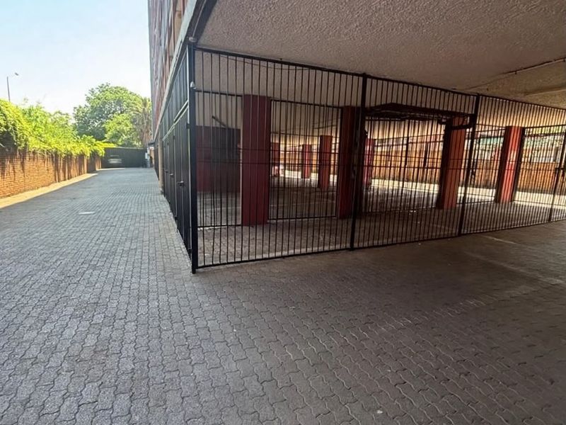 A secure, covered parking area featuring paved driveway access and metal security gating, situated alongside a brick boundary wall.