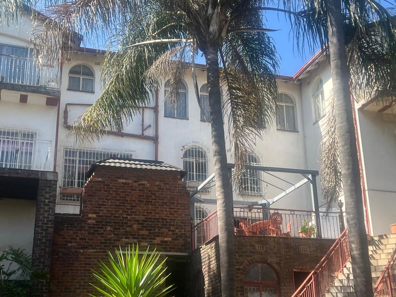 Rear elevation of a multi-story house featuring exposed brickwork, a raised patio area with metal railings, and arched window detailing.