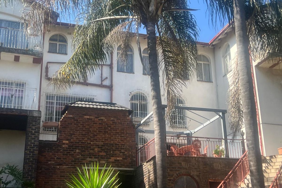 Rear elevation of a multi-story house featuring exposed brickwork, a raised patio area with metal railings, and arched window detailing.