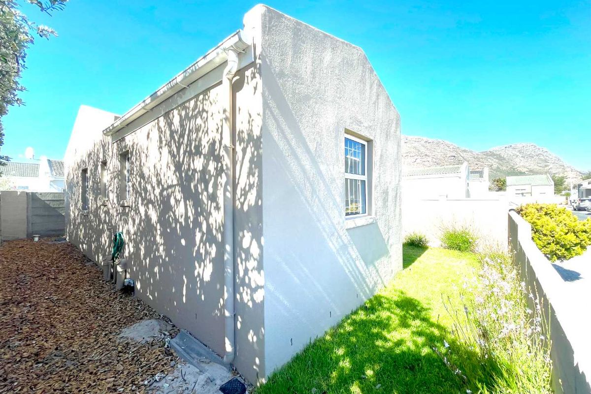 A view of the side exterior of the house featuring a rendered facade, guttering, and a small garden area with lawn.