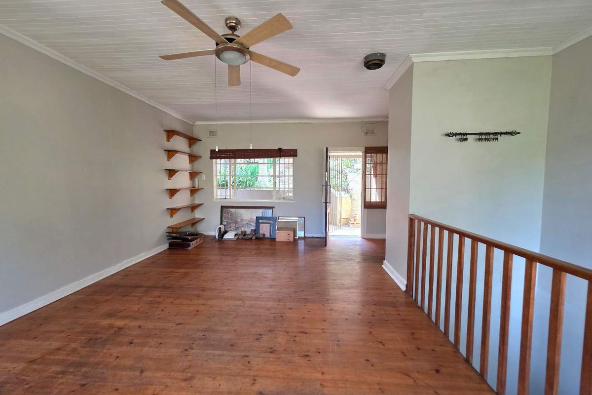 Spacious living area featuring polished timber flooring, a ceiling fan, built-in wall shelving, and direct access to an outdoor area.