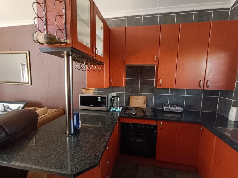 A functional kitchen featuring wood-finish cabinetry, granite countertops, a built-in oven and hob, and a breakfast bar with integrated wine storage.