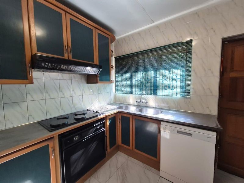 A functional kitchen featuring dark-toned cabinetry, a built-in oven and hob, stainless steel sink, and tiled finishes throughout.