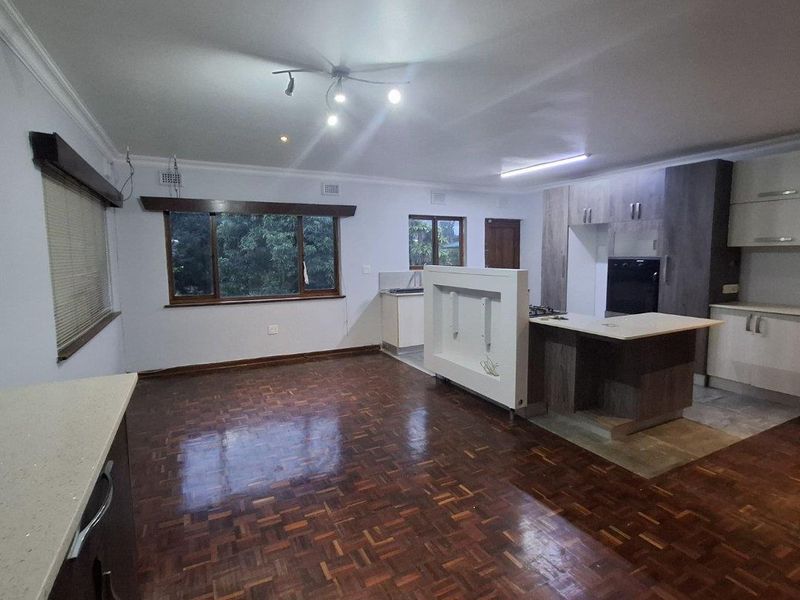 Spacious open-plan living and kitchen area featuring classic parquet flooring, modern cabinetry, and a central island, offering a versatile layout for dining and relaxation.