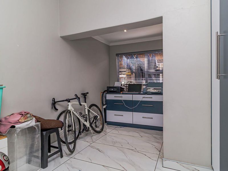 A functional office space featuring marble-look floor tiles, built-in cabinetry, and venetian blinds, providing a clean and versatile area for work or study.