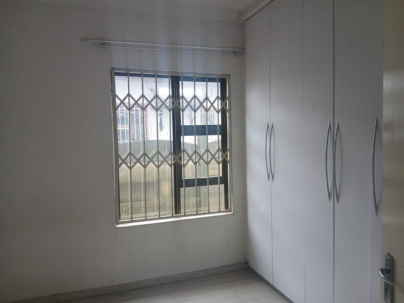 A vacant bedroom featuring built-in white cupboards and a window fitted with a security gate.