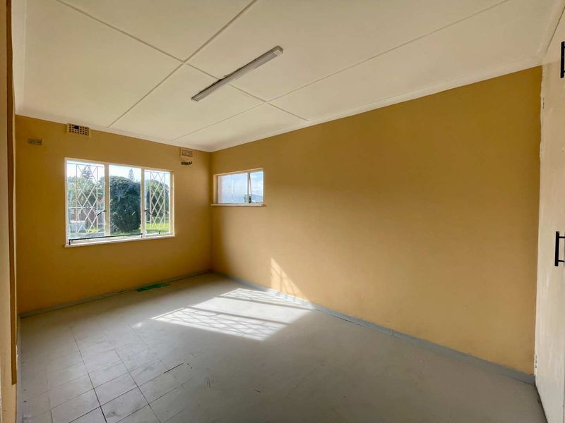 An empty bedroom featuring tiled flooring, security bars on the windows, and a built-in cupboard, offering a blank canvas for renovation.