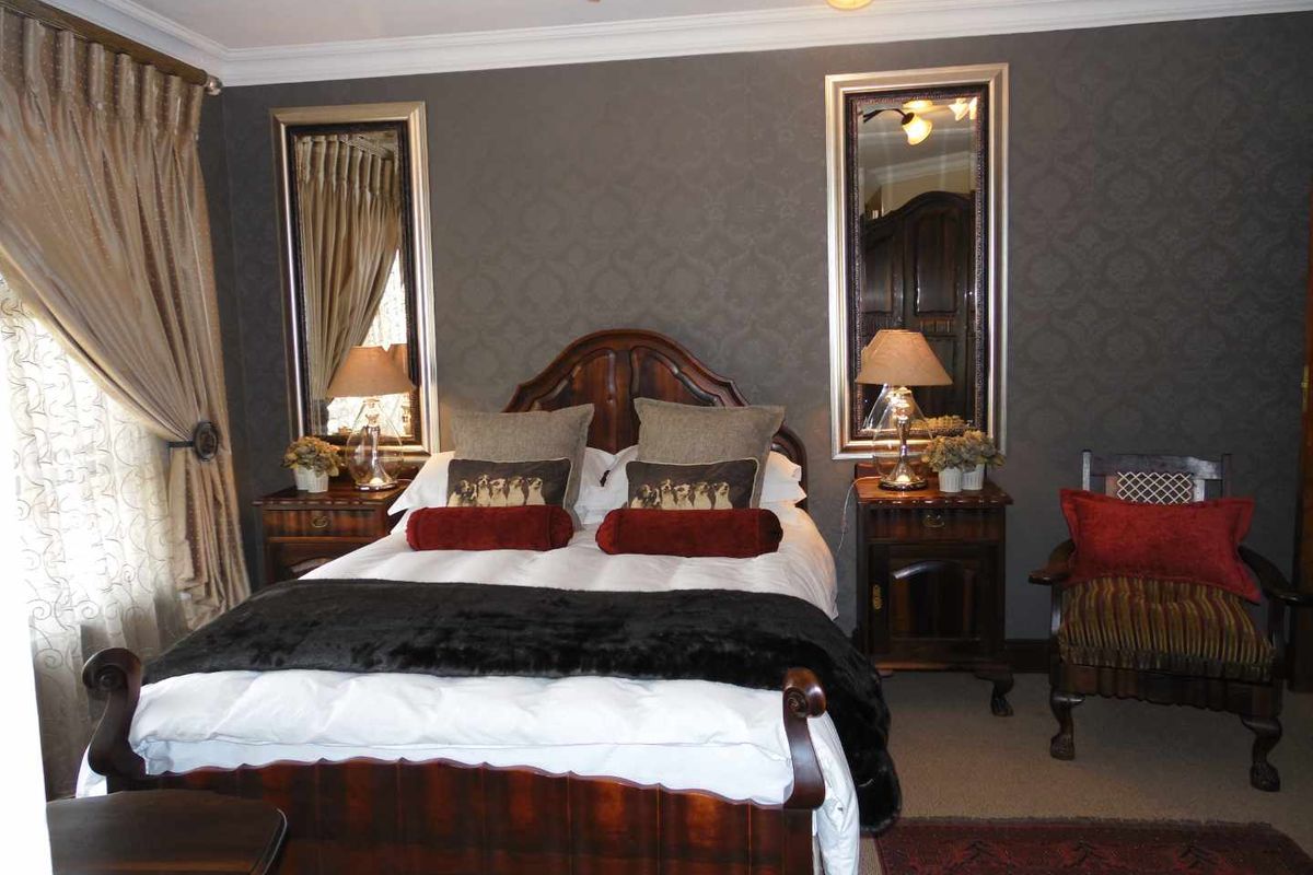 A well-maintained bedroom featuring dark patterned wallpaper, crown molding, and wall-mounted mirrors flanking the bed area.