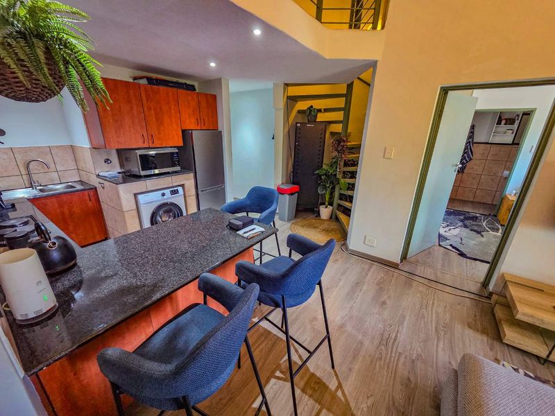 Open plan kitchen and living area featuring granite countertops, built-in cabinetry, laminate flooring, and a spiral staircase leading to the upper level.