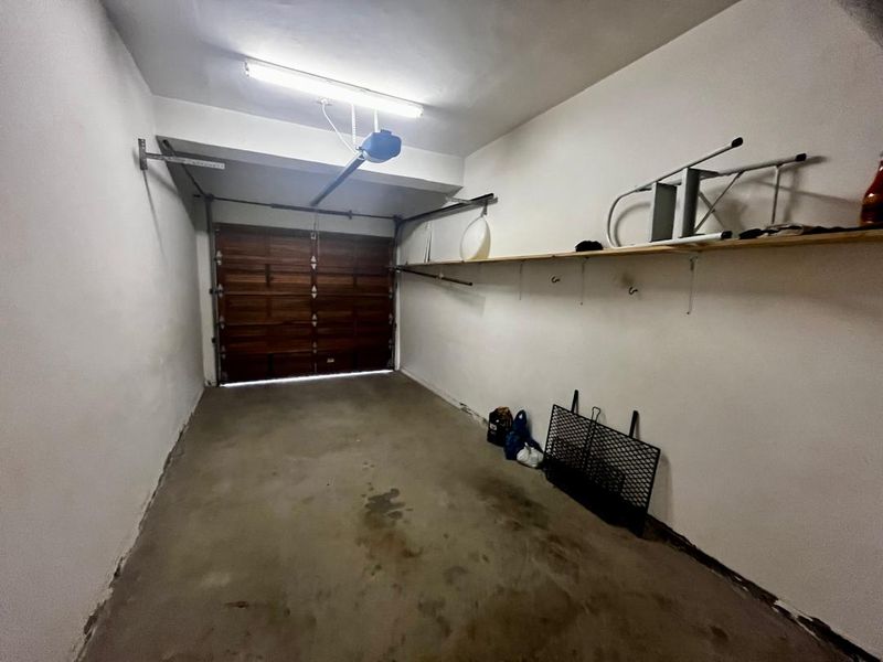 A functional single-car garage featuring a sectional door, overhead motor, and wall-mounted storage shelving with a concrete floor.