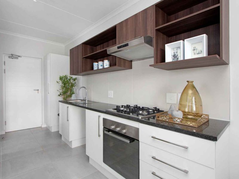 Modern kitchen featuring white base cabinets, dark wood overhead shelving, granite countertops, a gas hob, built-in oven, and stainless steel extractor fan.