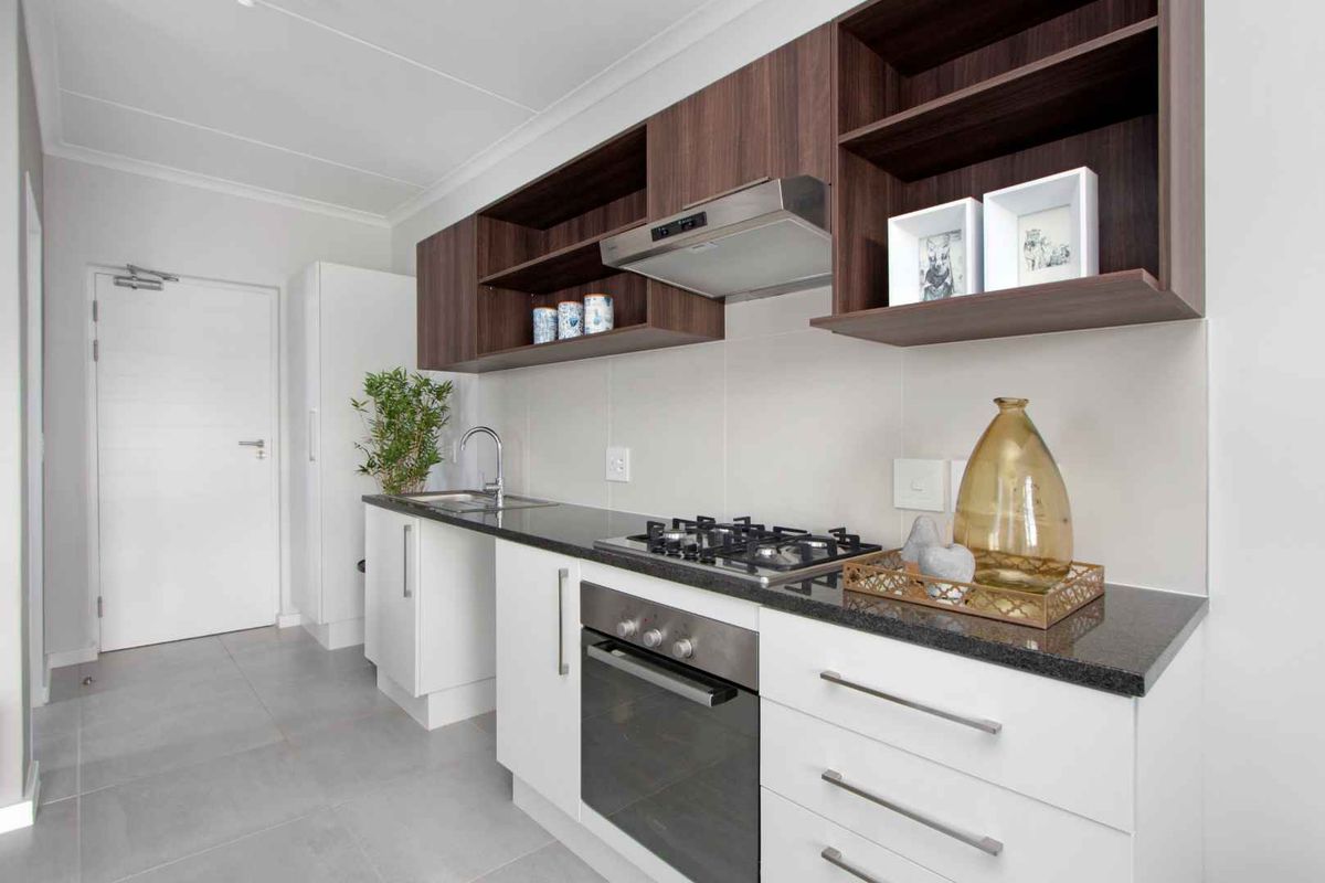 Modern kitchen featuring white base cabinets, dark wood overhead shelving, granite countertops, a gas hob, built-in oven, and stainless steel extractor fan.