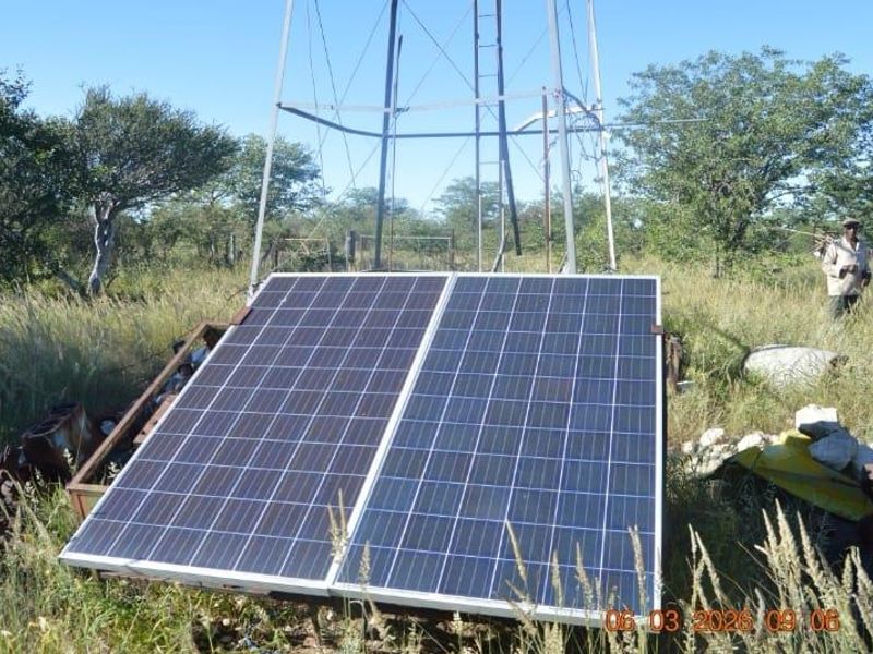 Outdoor utility area featuring a metal windmill structure and ground-mounted solar panels set within a rural farm landscape.