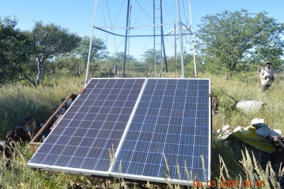 Outdoor utility area featuring a metal windmill structure and ground-mounted solar panels set within a rural farm landscape.