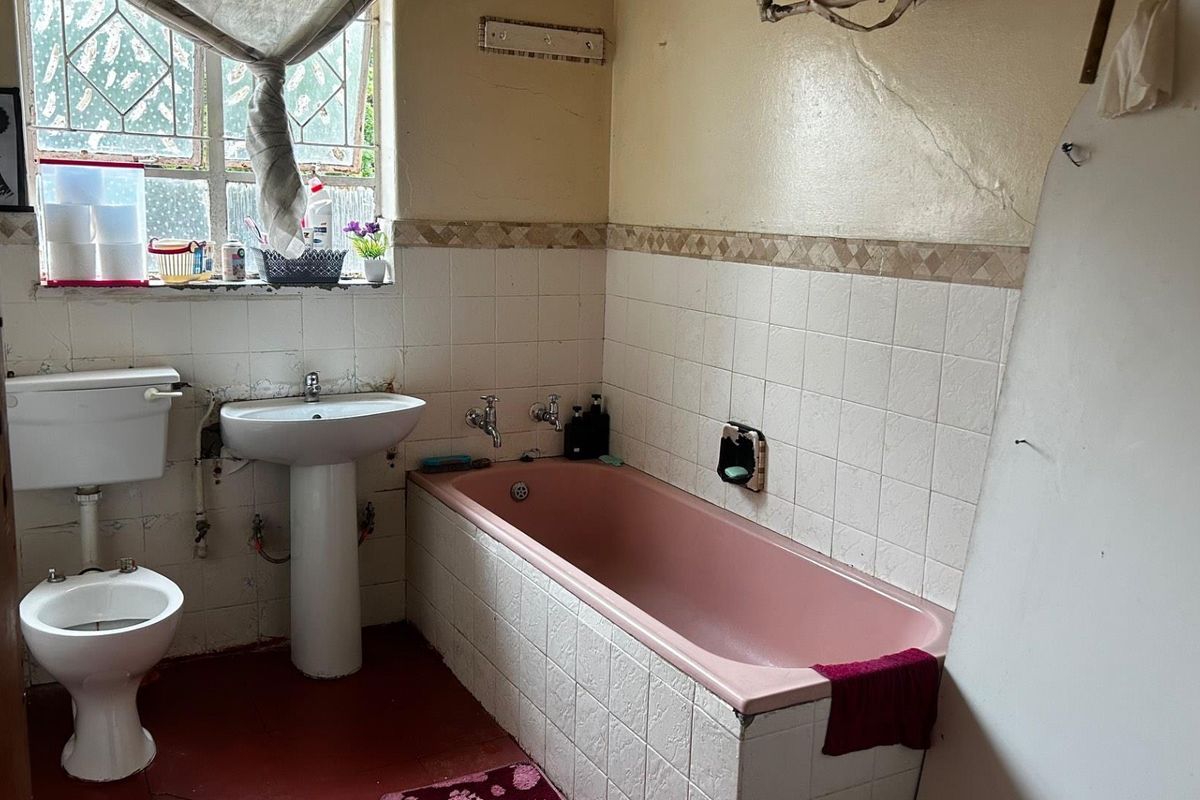 A dated bathroom featuring a pink bathtub, pedestal basin, and toilet, requiring significant renovation and modernization of finishes and fixtures.