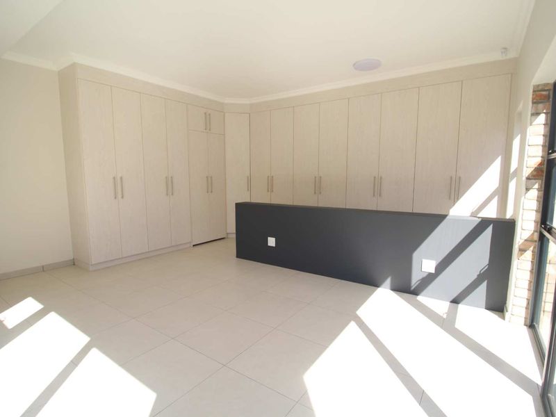 A bright, empty living area featuring extensive built-in cabinetry, neutral tiled flooring, and large glass doors providing natural light.
