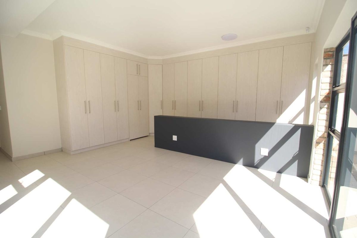 A bright, empty living area featuring extensive built-in cabinetry, neutral tiled flooring, and large glass doors providing natural light.