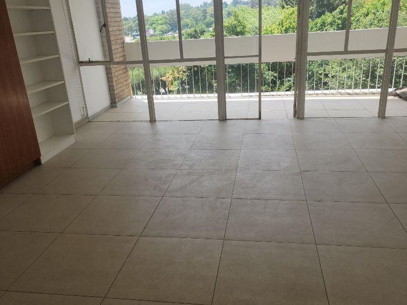 Spacious, light-filled living area featuring neutral floor tiles, built-in shelving, and large glass doors opening onto a balcony with scenic views.